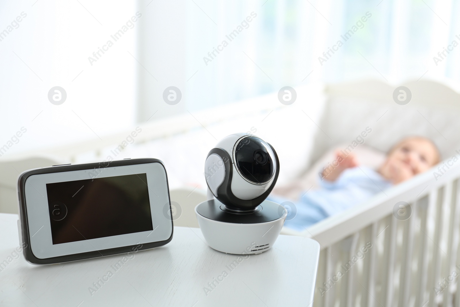 Photo of Baby monitor and camera on table near crib with child in room. Video nanny