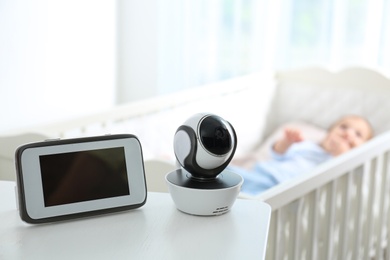 Photo of Baby monitor and camera on table near crib with child in room. Video nanny