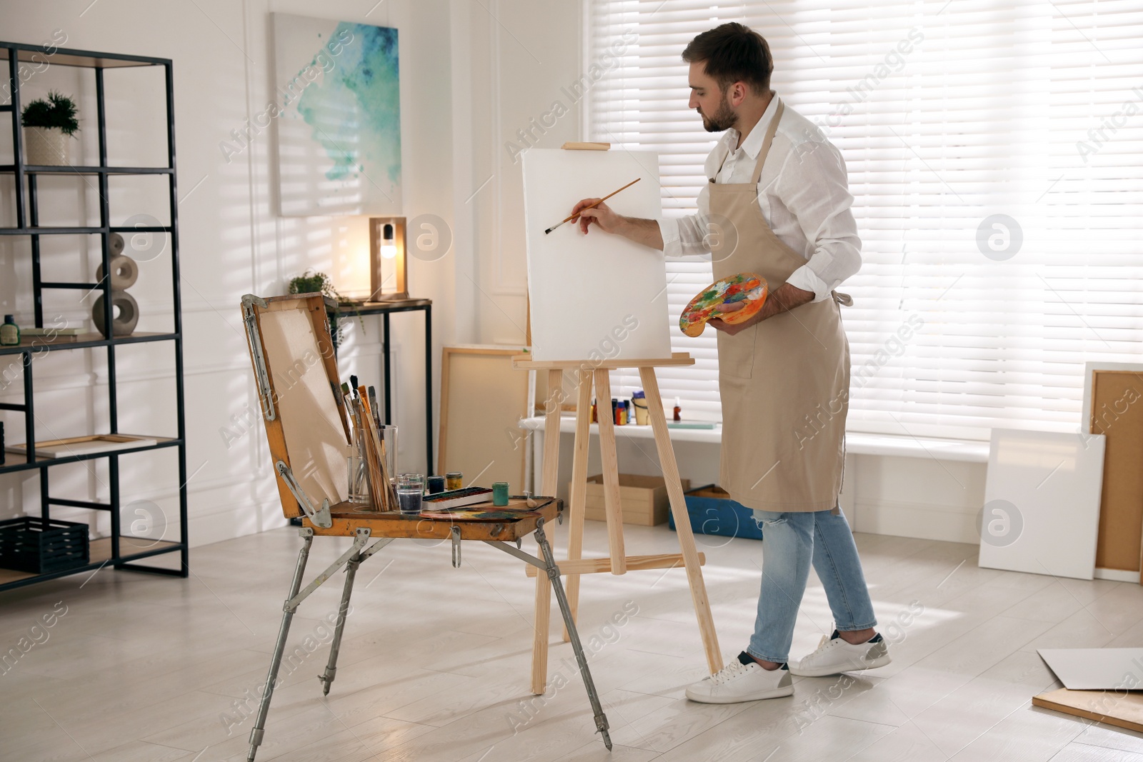 Photo of Young man painting on easel with brush in artist studio