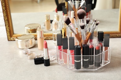 Photo of Lipstick holder with different makeup products on dressing table near mirror