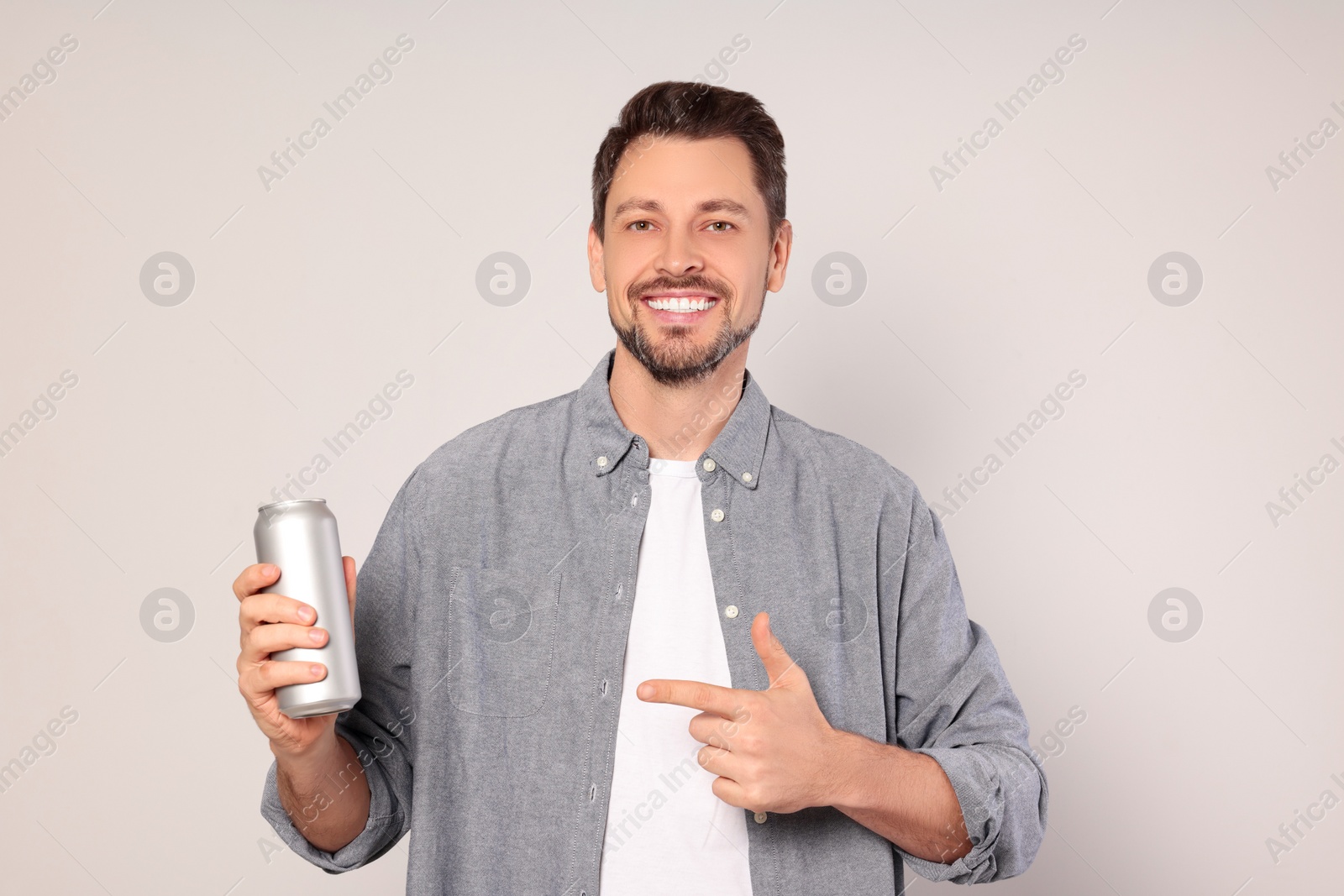 Photo of Happy man holding tin can with beverage on light grey background