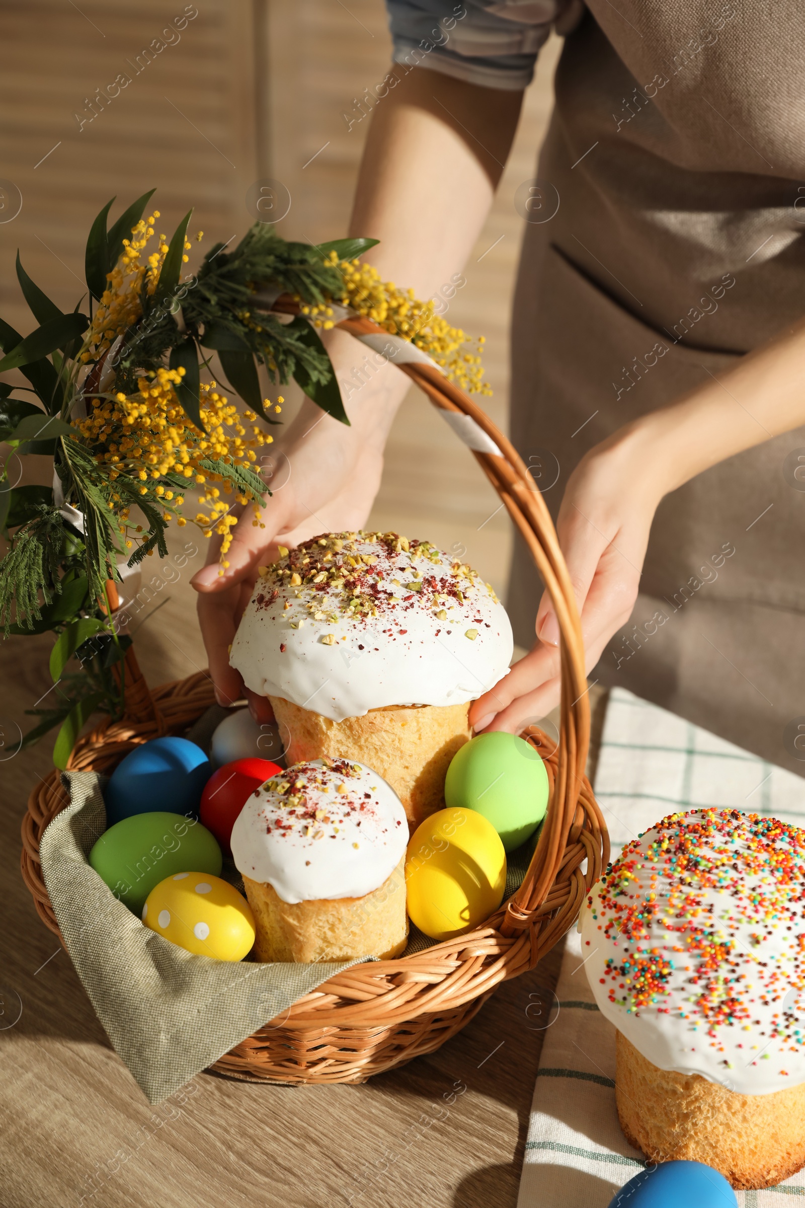 Photo of Woman putting traditional Easter cake in basket at table, closeup