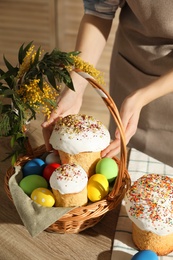 Woman putting traditional Easter cake in basket at table, closeup