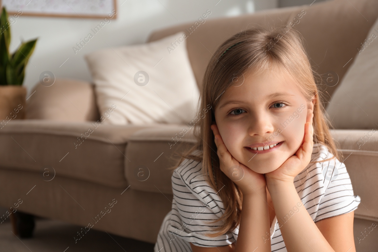 Photo of Cute little girl near couch at home. Space for text