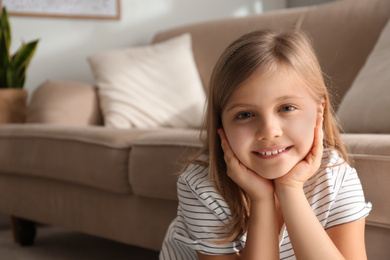 Photo of Cute little girl near couch at home. Space for text