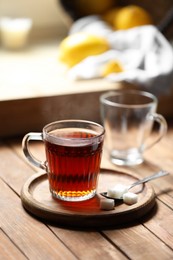 Photo of Glass cup with delicious tea and sugar on wooden table