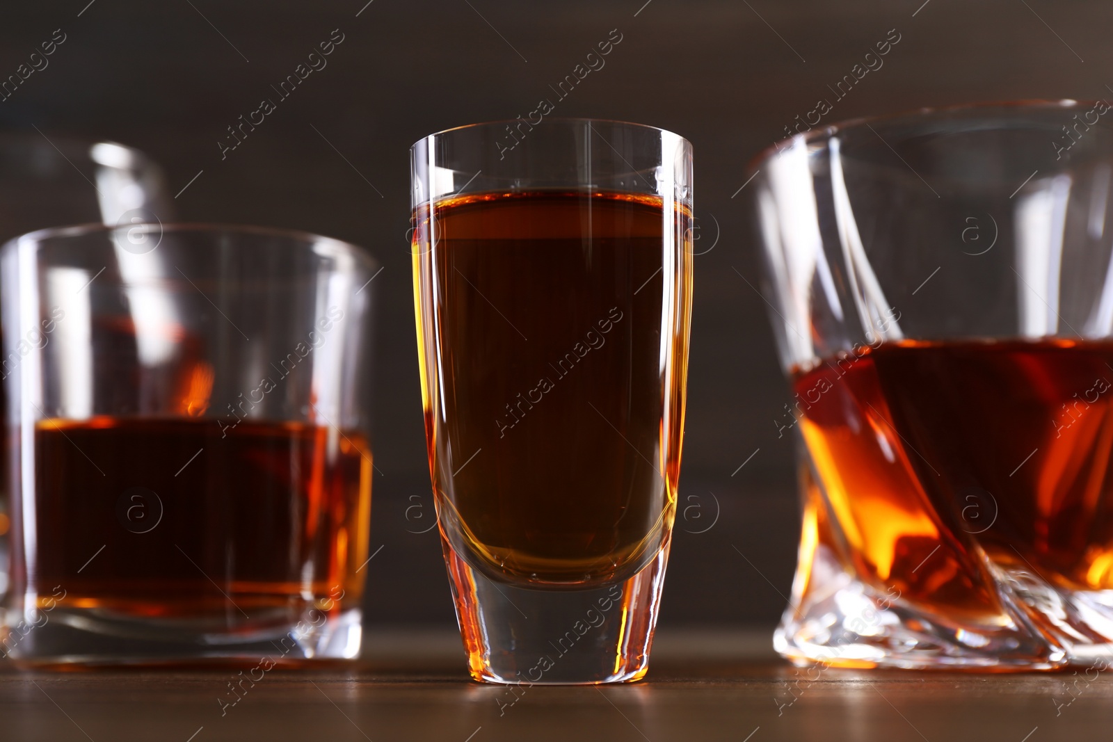 Photo of Different delicious liqueurs in glasses on wooden table