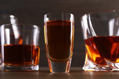 Different delicious liqueurs in glasses on wooden table