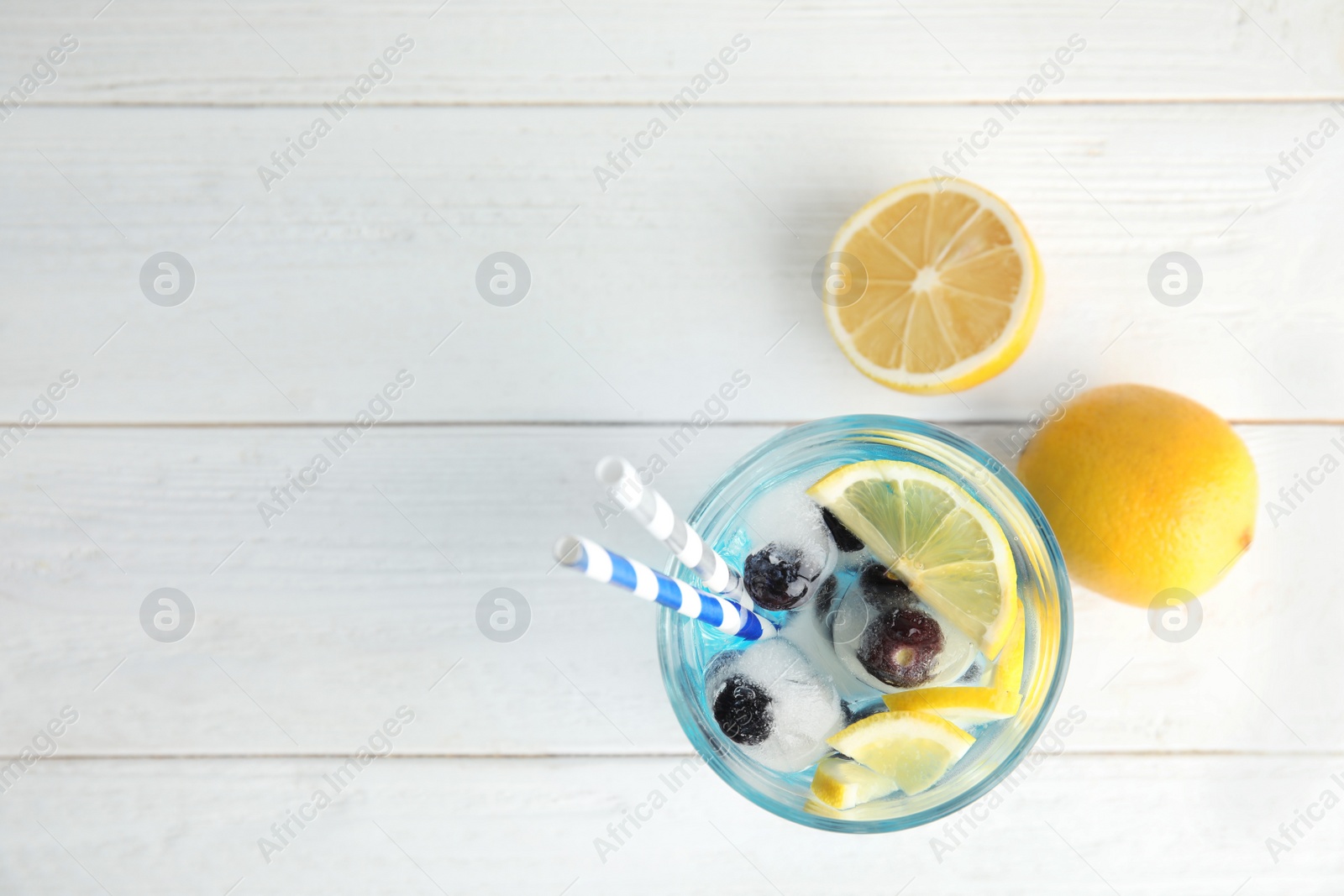 Photo of Tasty cocktail with blueberry ice cubes and lemons on wooden background, top view. Space for text