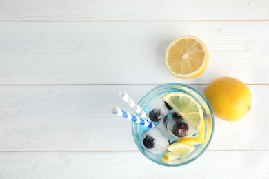 Tasty cocktail with blueberry ice cubes and lemons on wooden background, top view. Space for text