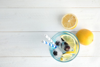 Photo of Tasty cocktail with blueberry ice cubes and lemons on wooden background, top view. Space for text