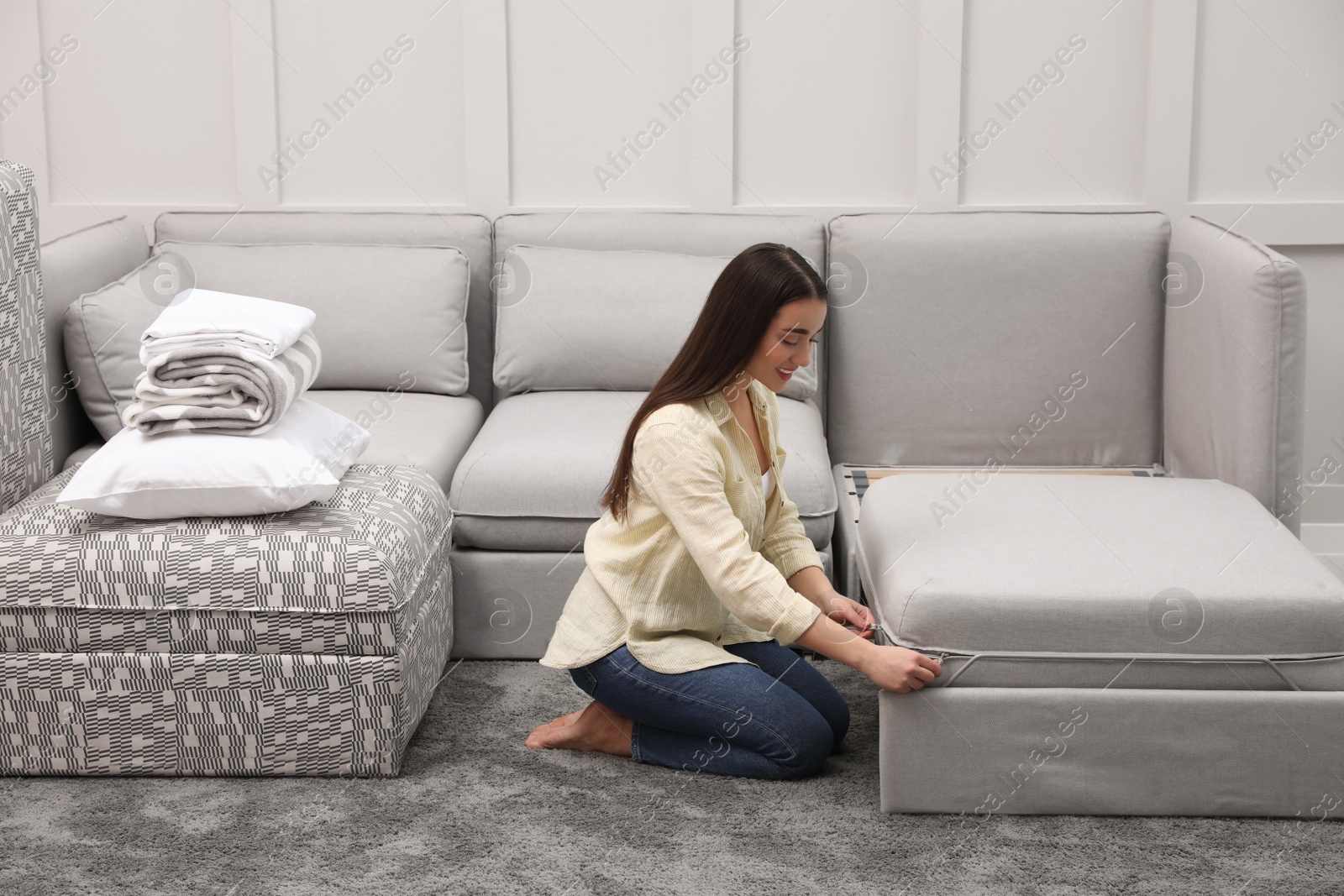 Photo of Woman making sleeping place for guest in living room. Convertible sofa