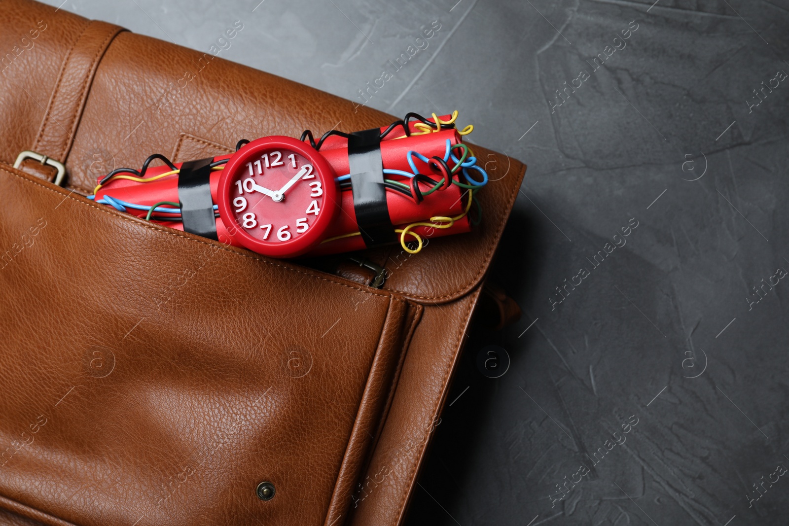 Photo of Leather briefcase with dynamite time bomb on grey table, top view. Space for text