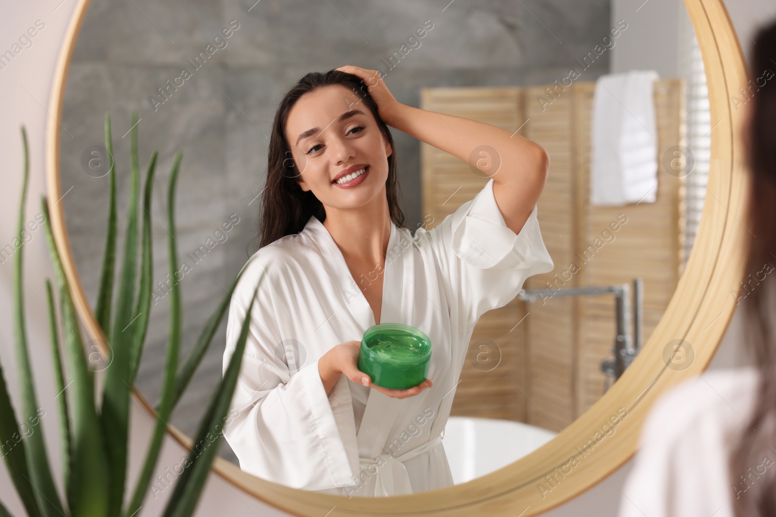 Photo of Young woman applying aloe hair mask near mirror in bathroom