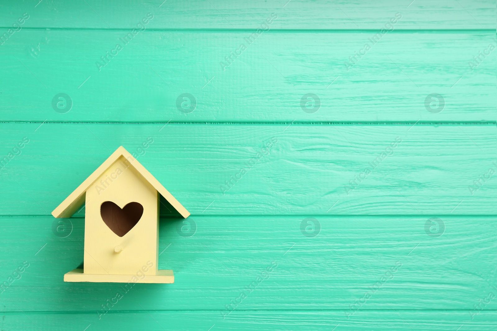 Photo of Beautiful bird house with heart shaped hole on turquoise wooden background, space for text
