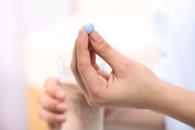 Photo of Woman holding pill and glass of water on blurred background, closeup. Space for text