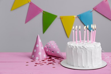 Photo of Delicious cake with burning candles and party hats on pink wooden table. Space for text