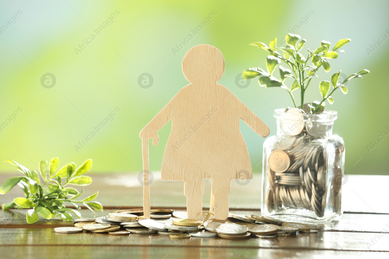 Photo of Pension savings. Figure of senior woman, coins and green twigs on wooden table against blurred background