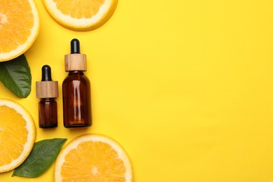Bottles of citrus essential oil and fresh orange slices on yellow background, flat lay. Space for text