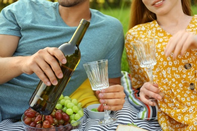 Photo of Young couple with wine and glasses having picnic outdoors, closeup