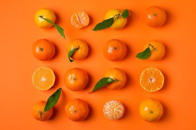 Photo of Delicious tangerines and green leaves on orange background, flat lay