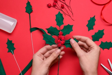 Photo of Woman making mistletoe branch on red background, top view
