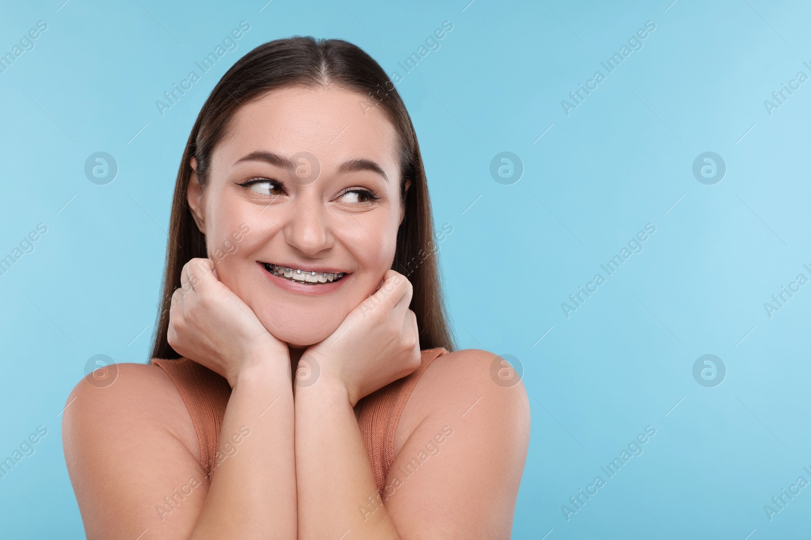 Photo of Smiling woman with dental braces on light blue background. Space for text