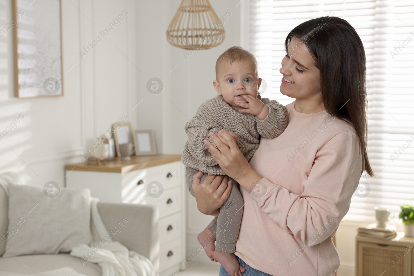 Photo of Happy young mother with her baby in living room. Space for text