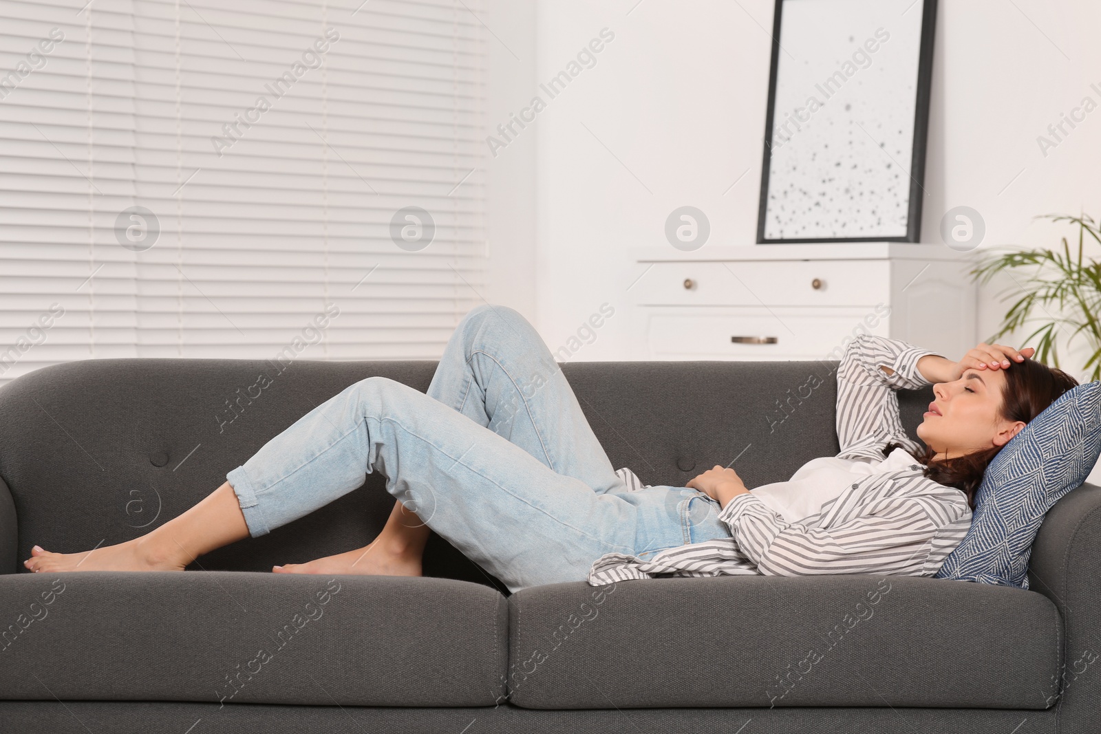 Photo of Young woman suffering from headache on sofa indoors. Hormonal disorders