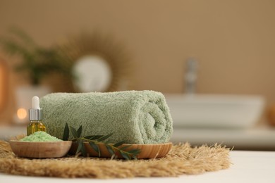 Photo of Spa composition. Rolled towel, cosmetic product, sea salt and twig on table indoors. Space for text