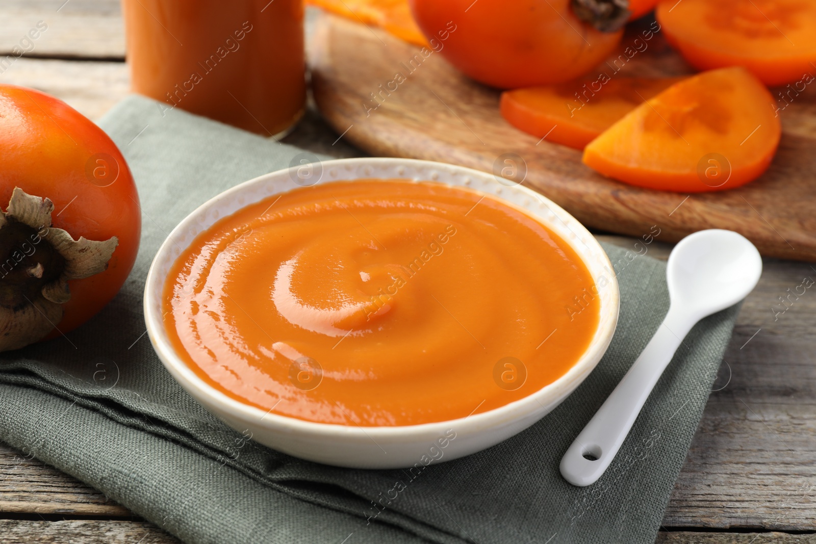 Photo of Delicious persimmon jam and fresh fruits on wooden table