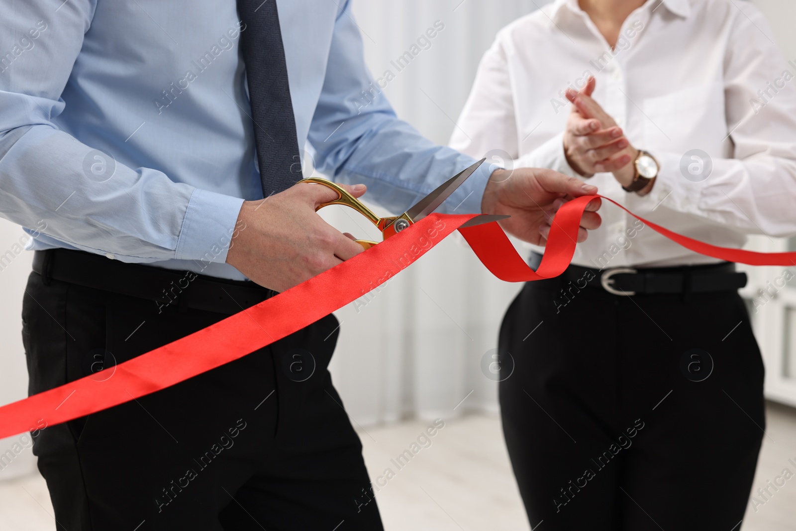 Photo of Man cutting red ribbon with scissors indoors, closeup