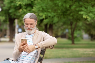 Photo of Handsome mature man with mobile phone sitting on bench in green park