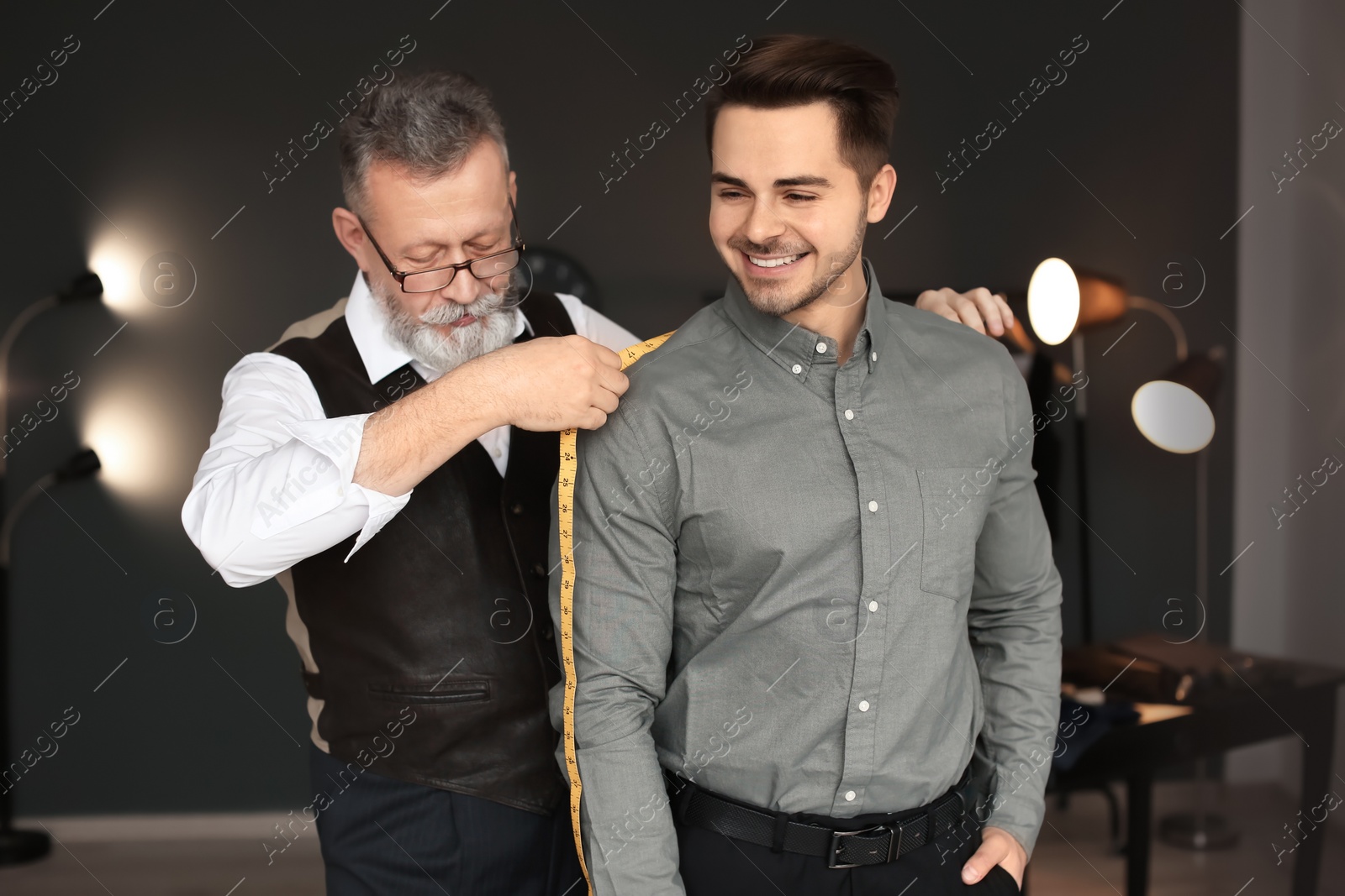 Photo of Mature tailor taking client's measurements in atelier