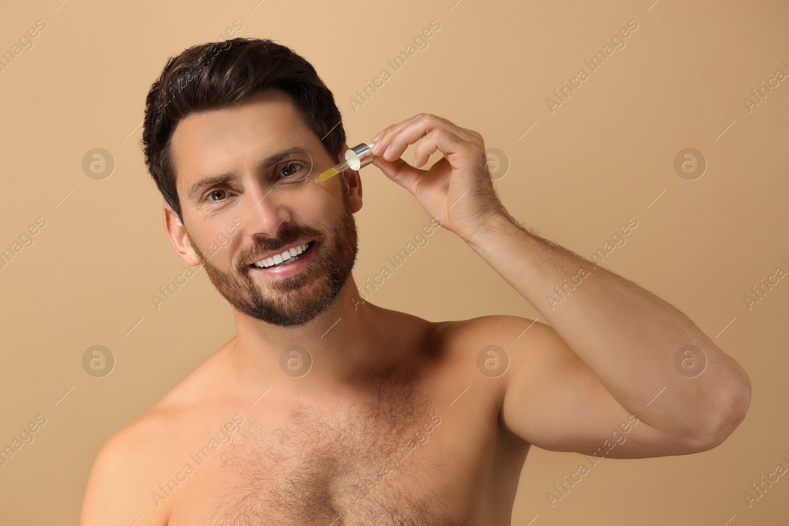 Photo of Smiling man applying cosmetic serum onto his face on beige background