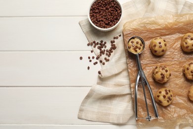 Photo of Uncooked chocolate chip cookies and scoop on white wooden table, flat lay. Space for text