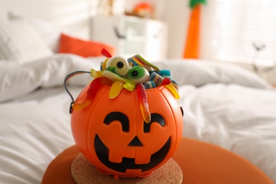 Photo of Halloween trick or treat bucket with different sweets on bed indoors