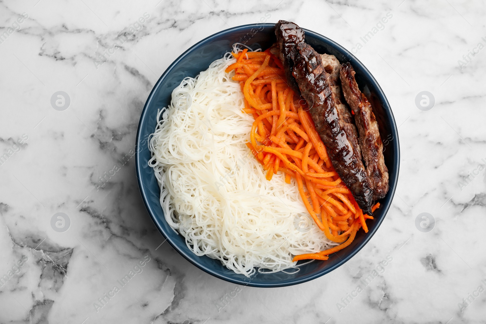 Photo of Tasty cooked rice noodles with meat and carrot on white marble table, top view