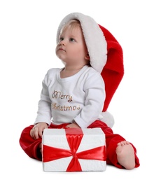 Photo of Cute baby in Santa hat and Christmas pajamas sitting near gift box on white background