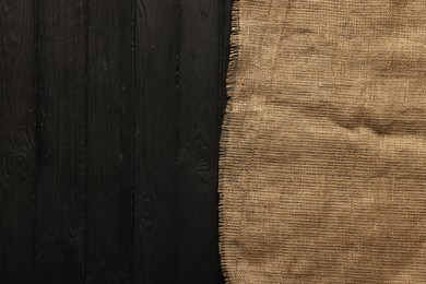 Burlap fabric on black wooden table, top view. Space for text