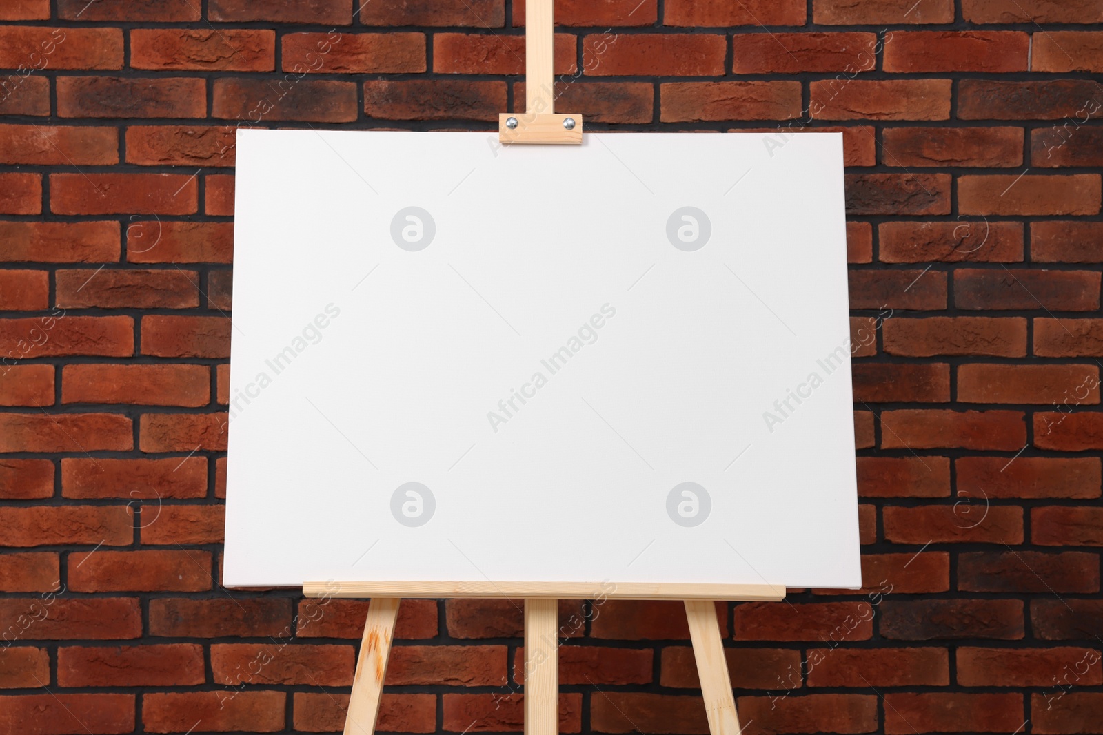 Photo of Wooden easel with blank canvas near brick wall, closeup