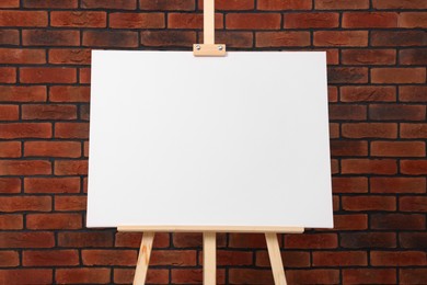 Wooden easel with blank canvas near brick wall, closeup