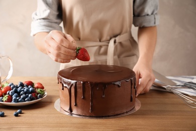 Photo of Baker decorating fresh delicious homemade chocolate cake with berries on table, closeup