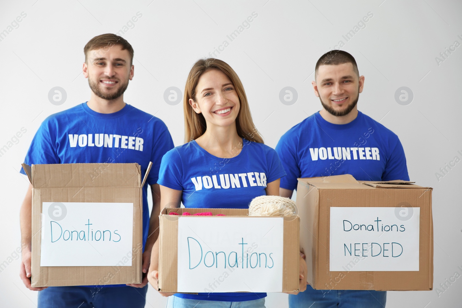 Photo of Young volunteers holding boxes with donations for poor people on light background