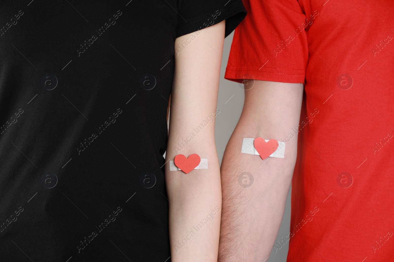 Photo of Blood donation concept. Couple with adhesive plasters on arms against grey background, closeup