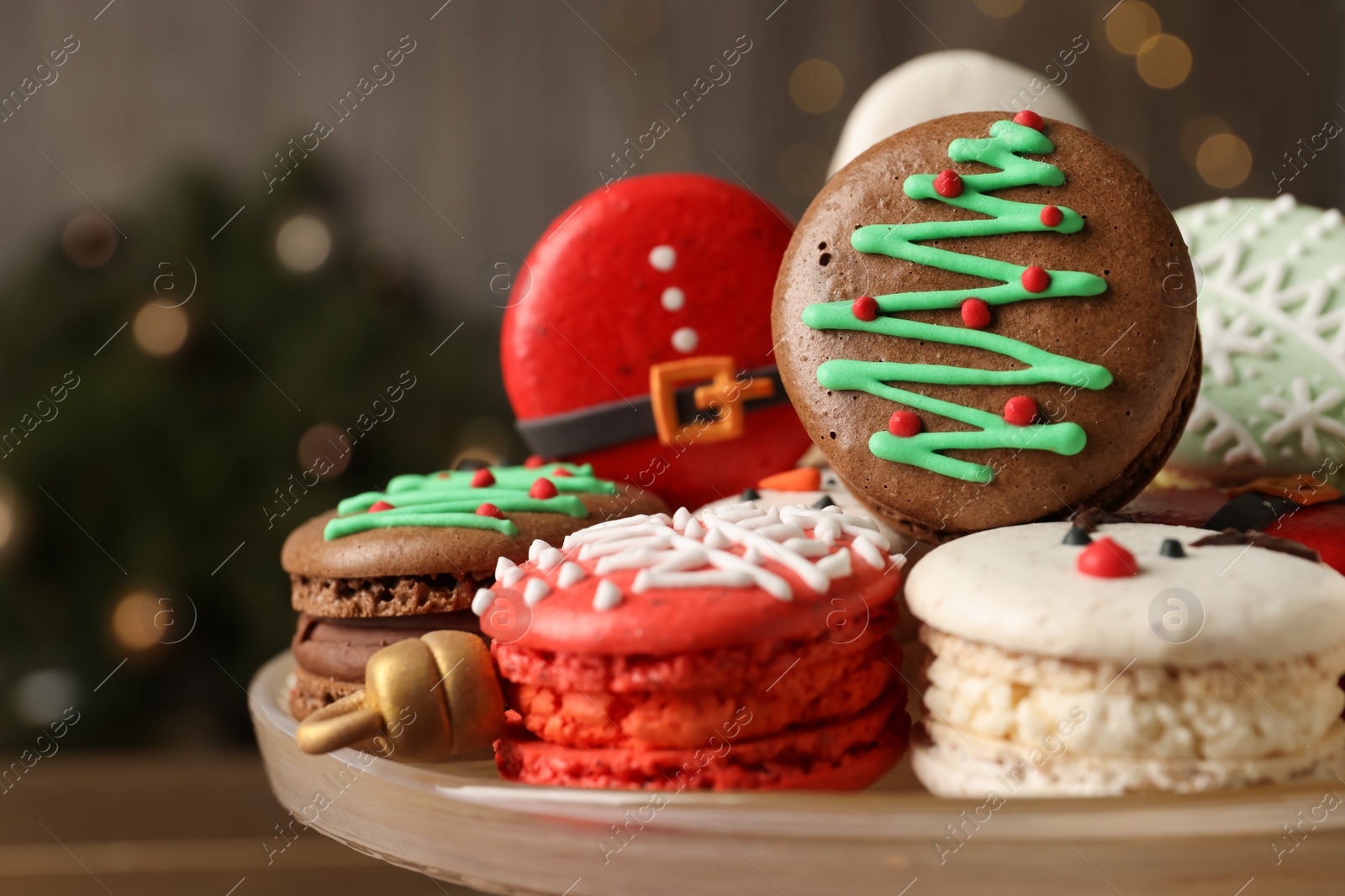 Photo of Beautifully decorated Christmas macarons on dish against blurred festive lights, closeup