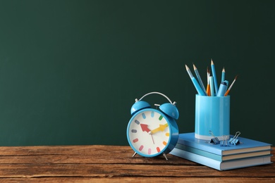 Photo of Alarm clock and set of stationery on wooden table near chalkboard, space for text. Teacher's Day