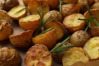 Photo of Tasty baked potato and aromatic rosemary on parchment paper, closeup