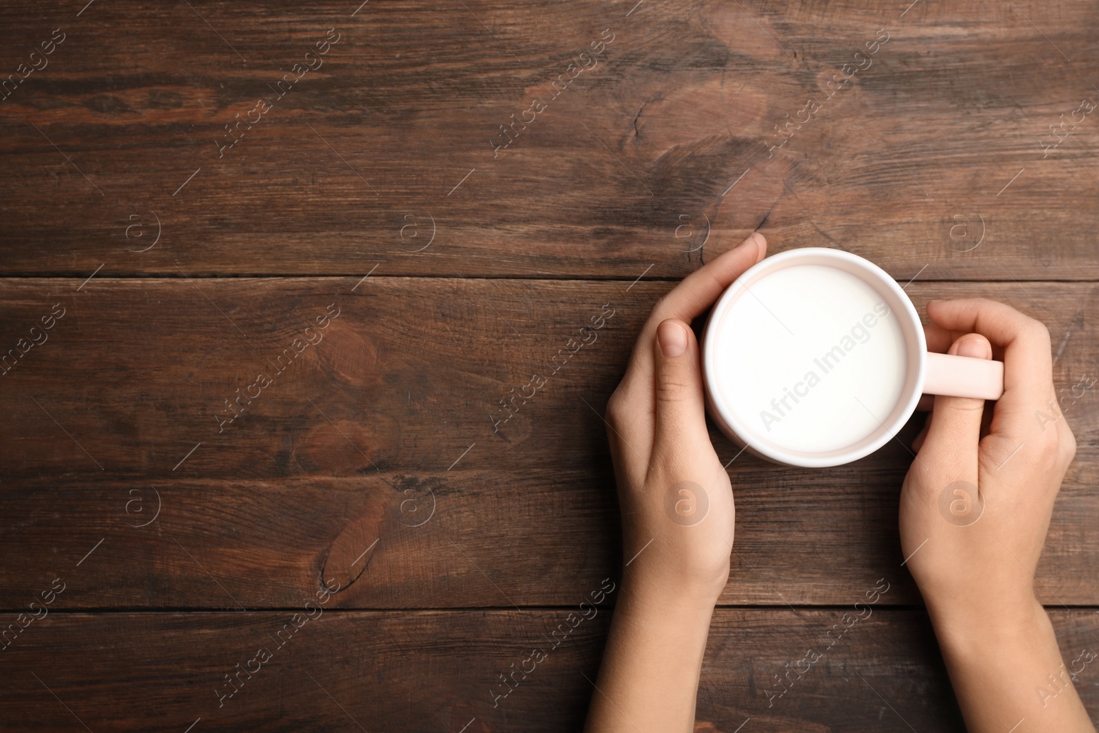 Photo of Woman holding cup of milk on wooden table, top view. Space for text