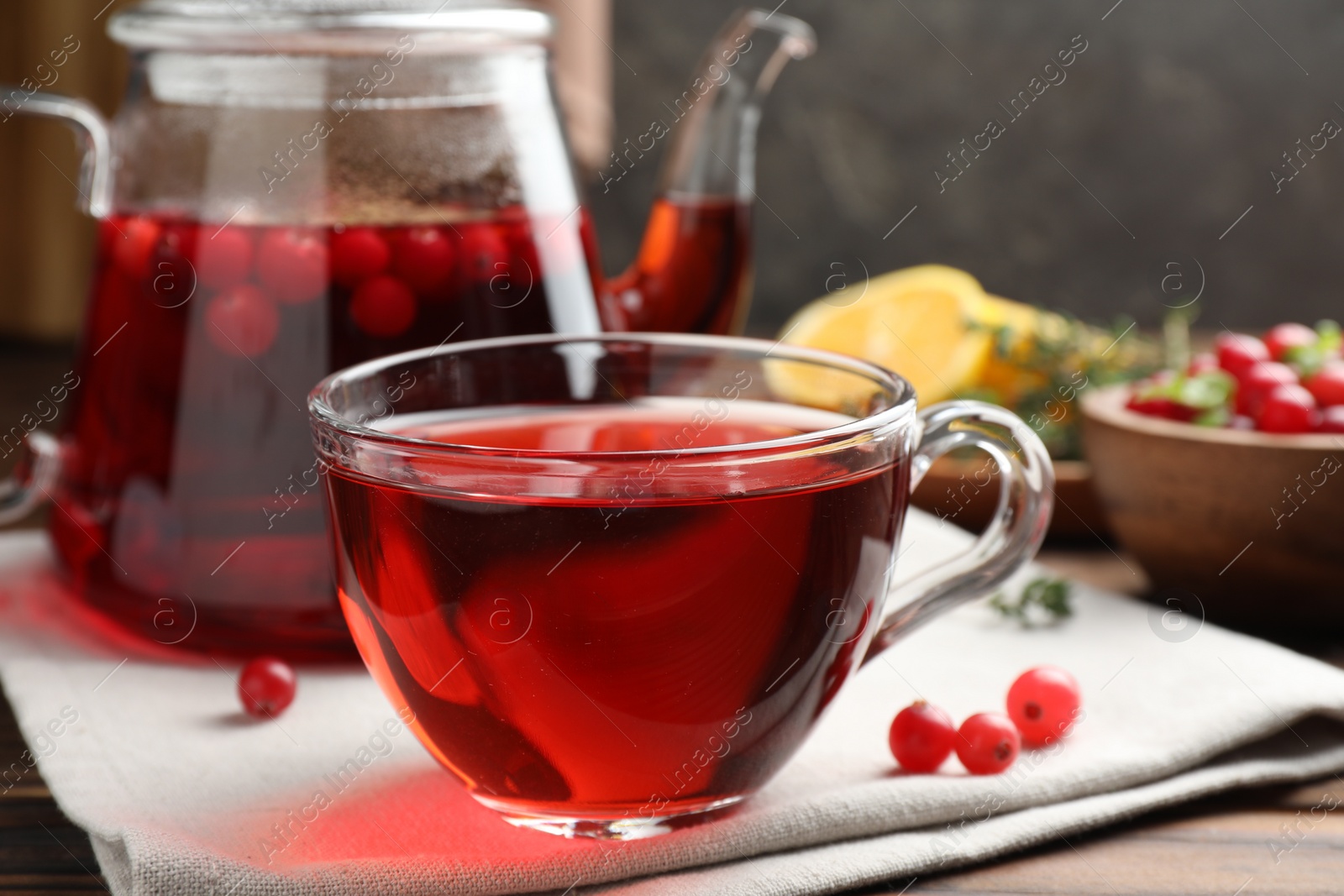 Photo of Tasty hot cranberry tea in glass cup and fresh berries on wooden table